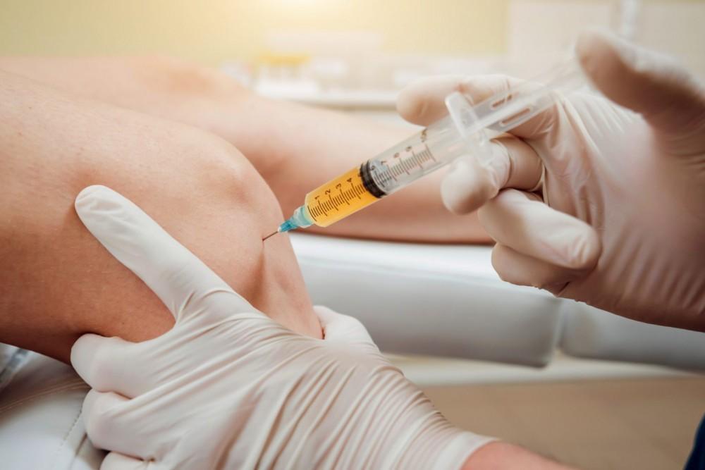 Clinician preparing an A2M joint injection for a patient with knee osteoarthritis in a modern Dallas medical clinic
