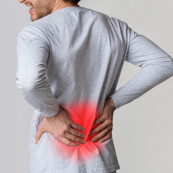 A person in a gray shirt holds their lower back with both hands, highlighting pain with a red glow, conveying discomfort and tension.