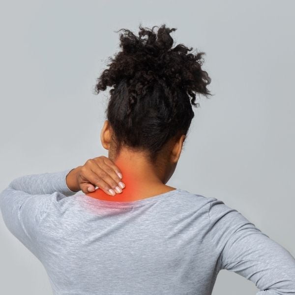 A person in a gray shirt with curly hair touches their neck, highlighting an area of red to indicate pain or discomfort on a neutral gray background.